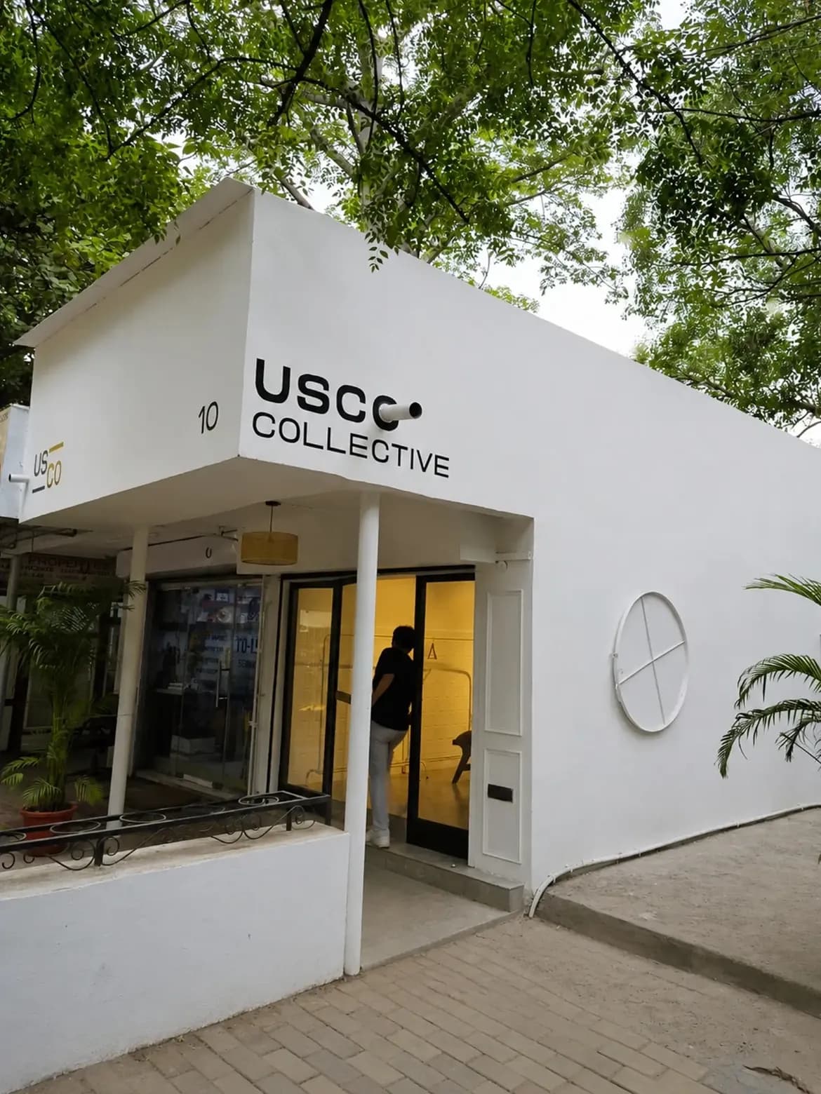 White exterior of the USCO Collective clothing shop surrounded by green trees.